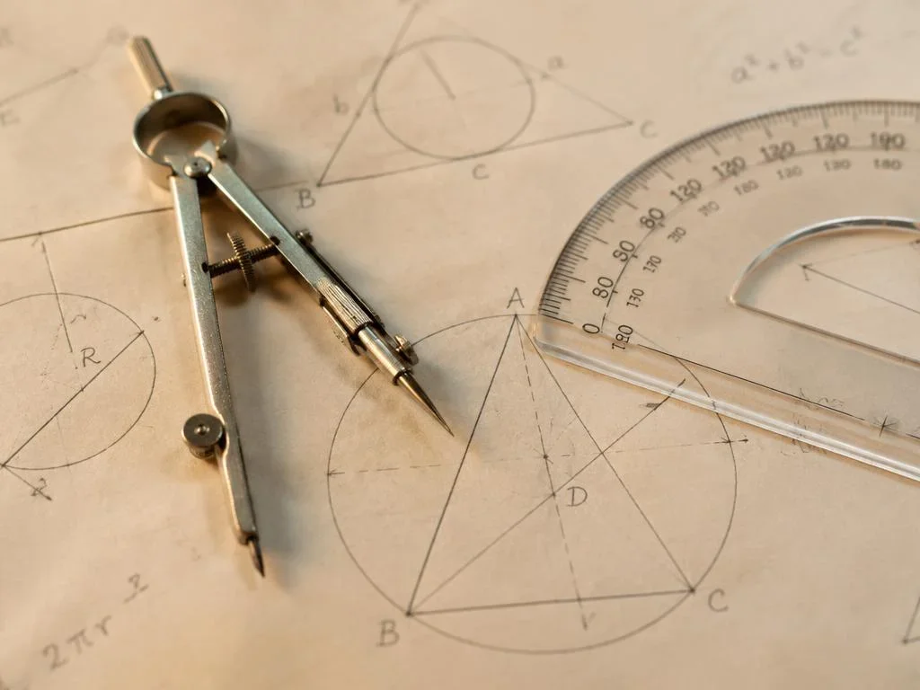 Compass and protractor resting over a hand-drawn geometry diagram
